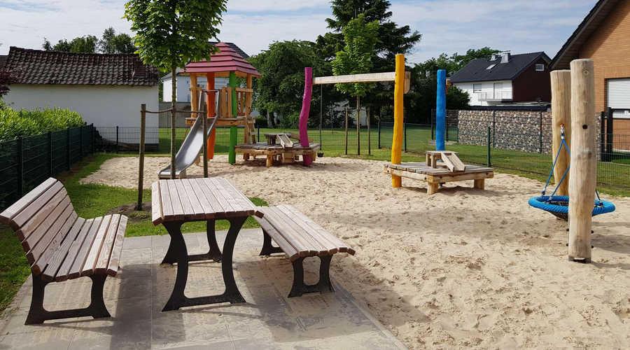 Blick auf den Spielplatz Lupinenweg mit Bänken und verschiedenen Spielgeräten