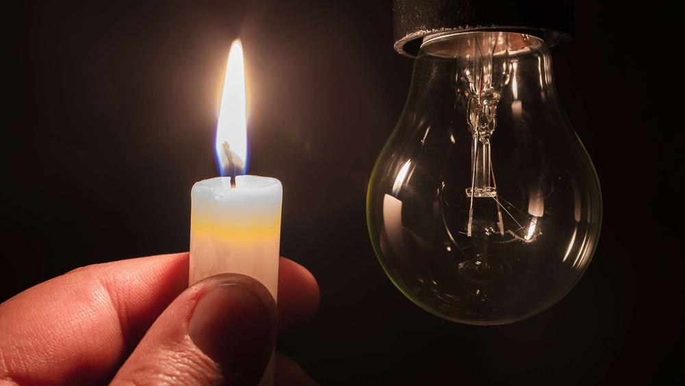 Eine Hand hält im Dunkeln eine Kerze vor eine dunkle Glühbirne