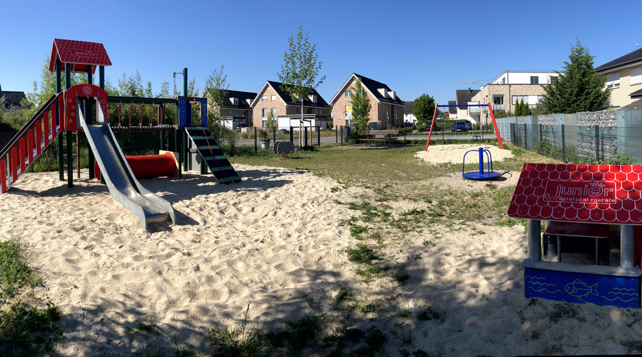 Blick auf Rutsche, Schaukel, Stehkarussel und Spielhaus