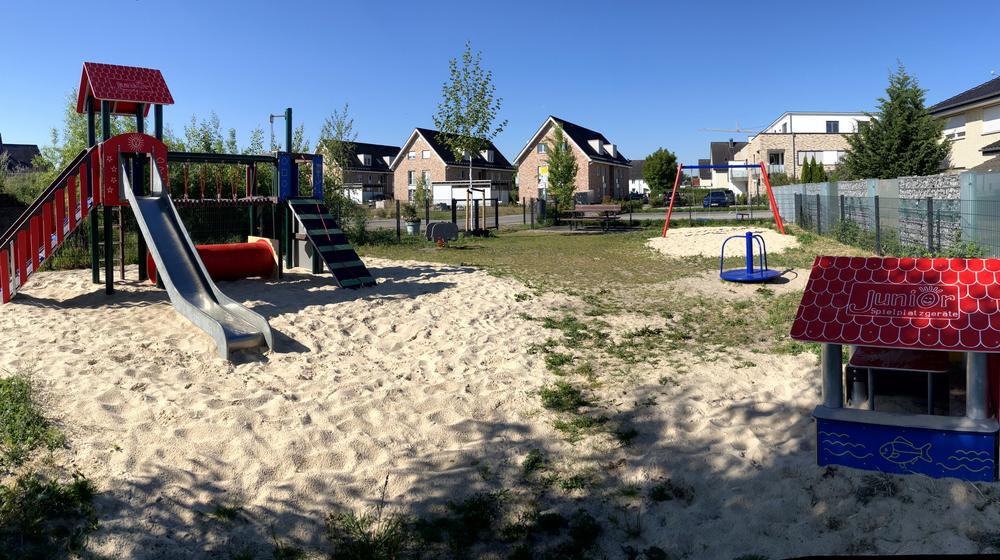 Blick auf Rutsche, Schaukel, Stehkarussel und Spielhaus